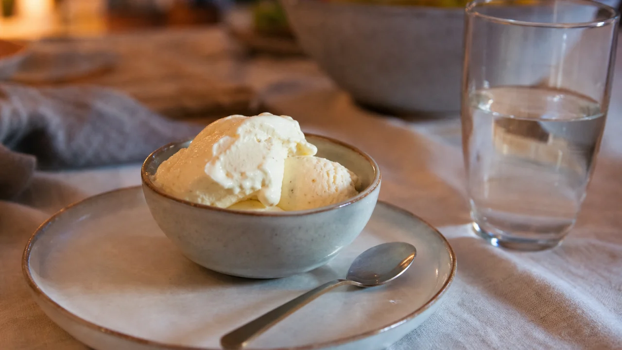 Coppetta di gelato alla vaniglia su un tavolo da cucina con bicchiere d’acqua in luce serale.