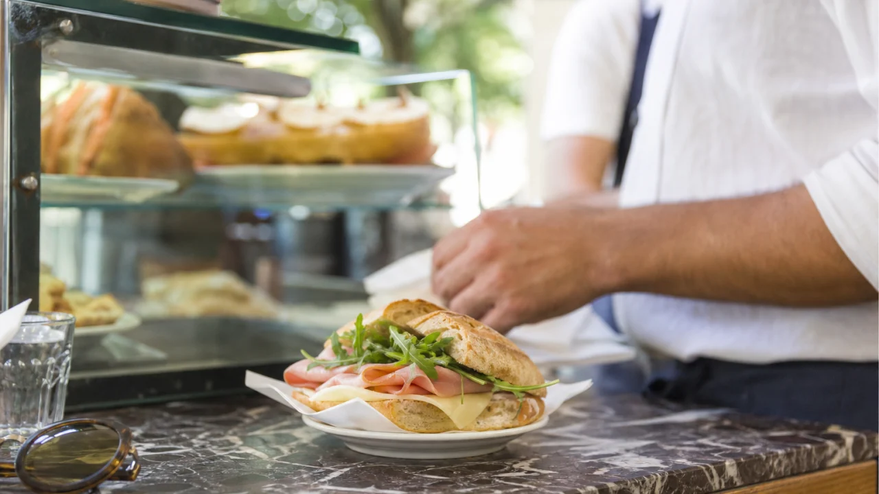 Panino fresco su bancone di bar italiano illuminato dalla luce estiva con vetrina sullo sfondo.